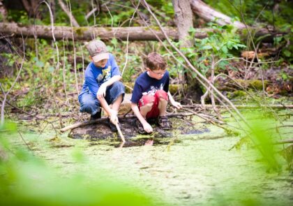 kuvituskuva, jossa kaksi lasta metsälammen rannalla.