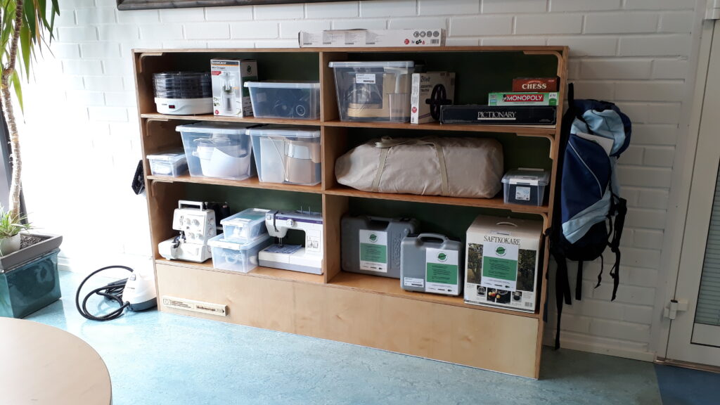 Shelf containing materials available for lending, like kitchen appliances, power tools and a sewing machine. 