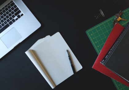 Kuvassa laptop-tietokone, vihkoja, kynä ja kirjoja.