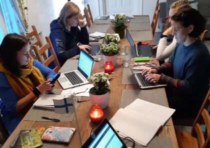 Kuva projektiryhmän neljästä jäsenestä työskentelemässä pödän ääressä kannettavilla tietokoneilla