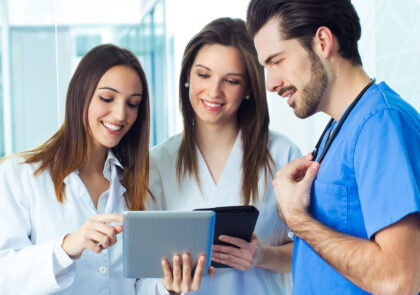 Kuvituskuva, jossa on hoitohenkilökuntaa, eli kaksi naista ja yksi mies. Naisilla on padit käsissä ja he katsovat tietoja niiden näytöiltä.