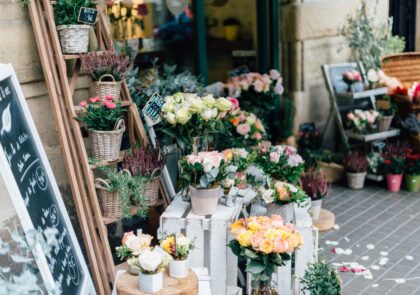 Valokuva kukkakaupan edustalta, jossa kadulle on aseteltu erilaisia kukkakimppuja ja kukka-asetelmia.