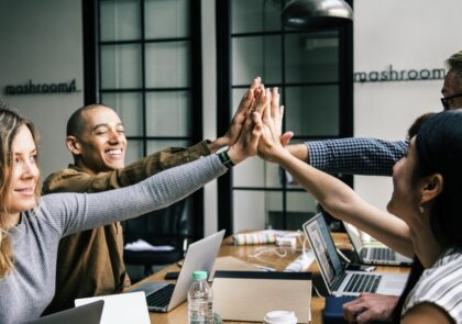 Neljä ihmistä lyö kätensä yhteen työpöydän äärellä.