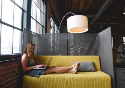 Nainen työskentelemässä keltaisella sohvalla kannettava tietokone sylissään.