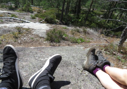 Kuvituskuva kallioilla istuvien henkilöiden jaloista