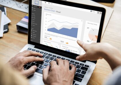 Kuvituskuva, jossa näkyy tietokoneen ruudulla erilaisia tilastoja. Yhden ihmisen kädet työskentelevät näppäimistöllä ja toisen ihmisen käsi osoittaa tilastoja.