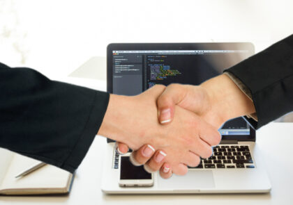 Kuvituskuva jossa kaksi kättä kättelevät. Taustalla näkyy kannettava tietokone.