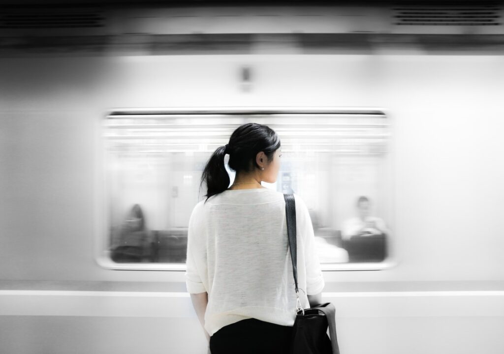 Photo of a woman standing in front of a moving subway train.