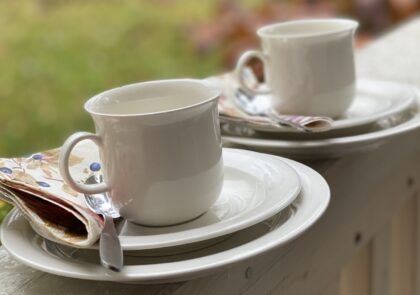 Kuvassa kaksi kahvikuppia aluslautasineen ulkona terassin kaiteella.