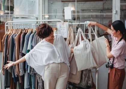 A photograph of two women looking at textile bags hanging together with other clothes on a hanging rail.