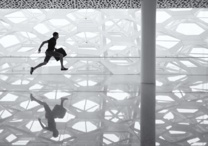 Peilipintainen, vaalenharmaakuvioitu tila, jonka keskellä mies juoksee laukku kädessään.