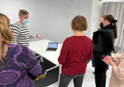 Kuvituskuvassa on pieni ryhmä ihmisiä, jotka katsovat pöydällä olevan kannettavan näyttöä.