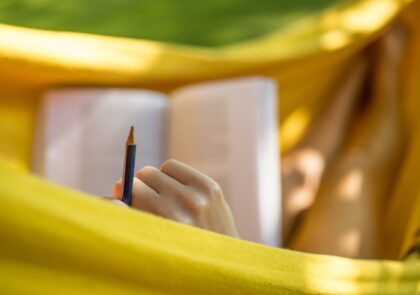 Keltainen riippukeinu, jossa henkilö lukee kirjaa lyijykynä kädessään.