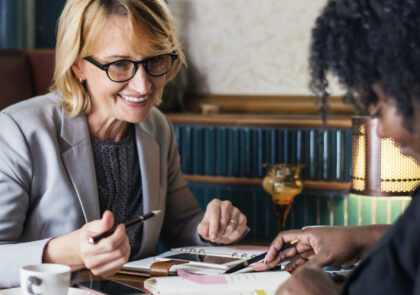 Kuvituskuvassa kaksi ihmistä istuu saman pöydän ääressä vastapäätä toisiaan ja katsovat paperisia kalentereitaan.