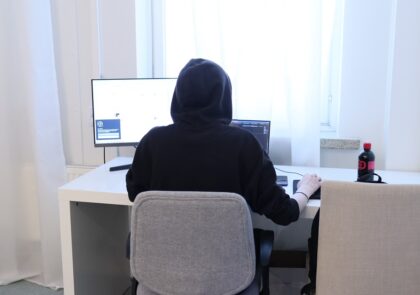 takaa kuvattu kuva huppu päässä tietokoneen ääressä istuvasta henkilöstä