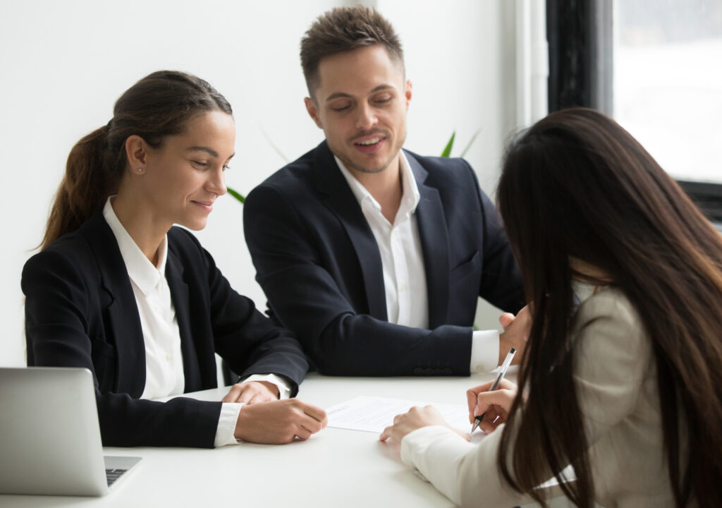 Illustration shows three people sitting around a table. One of them writes her name on the employment contract.