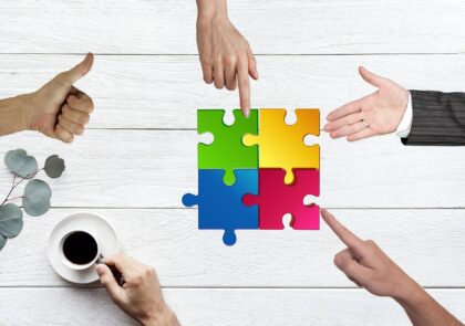 Kuvituskuvassa pöydällä on neljä värikästä palapelin palaa, joita kahden käden etusormet ja yksi kämmen osoittavat. pöydällä on myös kahvikuppi, josta ihmisen käsi pitää kiinni ja toisella kädellä näytetään peukkua.