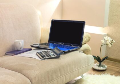 Kuvituskuvassa sohva, jolla kannettava tietokone, taskulaskin ja kahvikuppi.