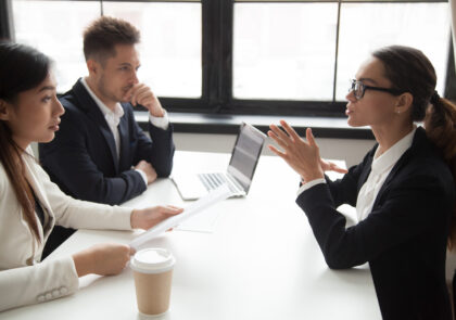 Kuvituskuvassa kolme ihmistä istuu toimistossa pöydän ääressä ja keskustelee.