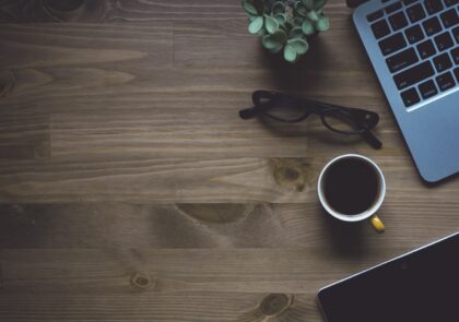 Kuvituskuvassa pöydällä on tietokone, kupillinen kahvia ja pieni viherkasvi.