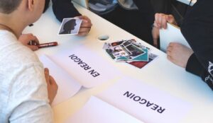 Kuva on pöydästä jonka ääressä osallistujat järjestävät kuvia ryhmiin, jotka on lapuilla nimetty Reagoin ja En reagoi. 