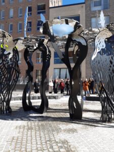 Etualalla korkea, neliosainen abstrakti veistos, jonka takana ryhmä ihmisiä.