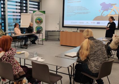 Joukko ihmisiä istuu pöydän ääressä selin kameraan ja seuraa diaesitystä.