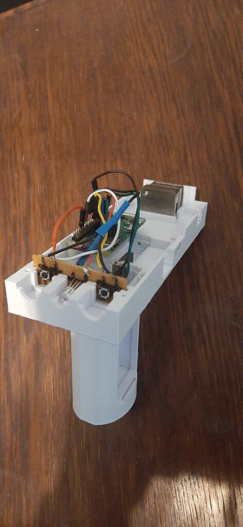 Kuva esittää pistoolimaista käsiskanneria ilman kansiosaa paljastaen laitteen sisällön. Kuvassa näkyy Nirone-sensori, joka on kytketty Raspberry Pi Zero -piirikorttiin. Lisäksi etualalla on nähtävissä kaksi kytkintä sekä yksi ledi niiden välissä, jotka on myös kytketty Raspberry Pi -korttiin.