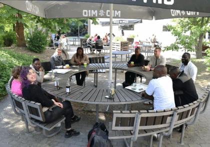 A group of people sitting outside around a round table.