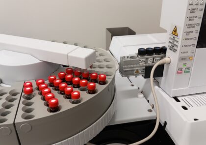 Analyysilaite, pyöreä näytetarjotin, punakorkkisia ajopulloja, robottivarsi, näytteensyöttötorni.