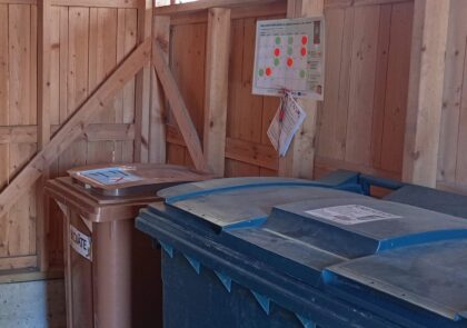 Biojäteastia jätekatoksen perällä ja seinällä lajittelunaapurin arviointikalenteri.