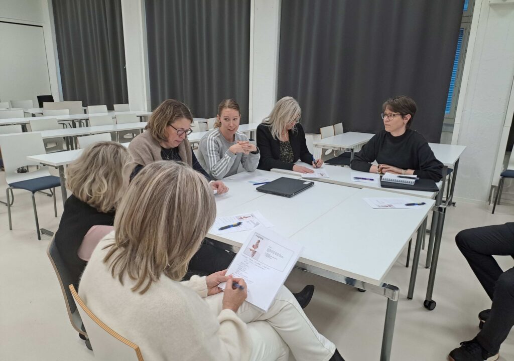 Kuvassa seitsemän henkilöä keskustelee pienryhmänä tehden muistiinpanoja koulutuksesta annettuun materiaalipohjaan