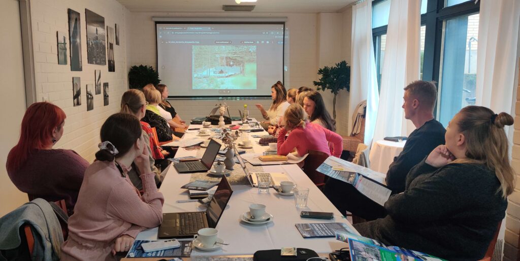 Joukko ihmisiä istuu pöydän ääressä selin kameraan ja seuraa valkokankaalle heijastettua esitystä. 