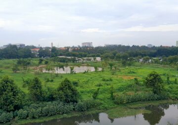 A very lush green park within a partly built up area in Vietnam. There is a pond in the foreground and another further in the background.
