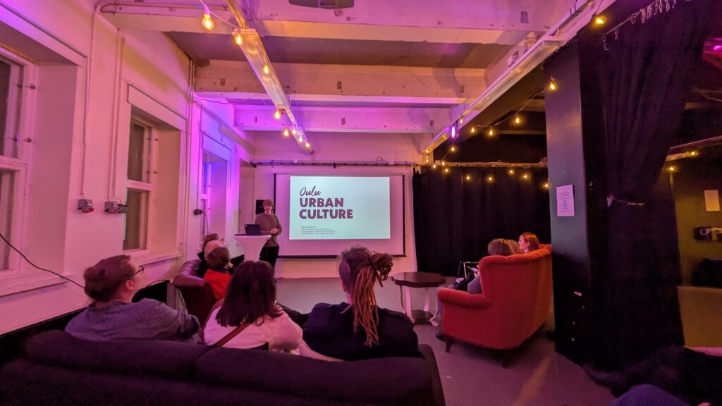 Joukko ihmisiä istuu katsomassa luentoesitystä.