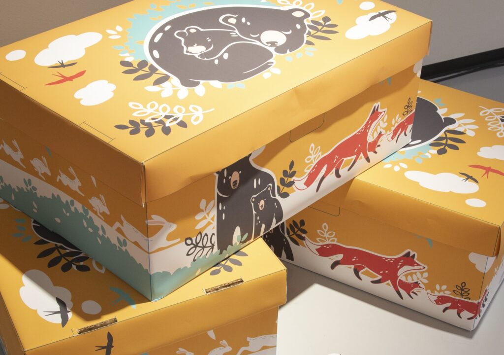 Pahvisia Kelan äitiyspakkauksia. Äitiyspakkaus on perinteinen suomalainen äitiysavustuslaatikko, joka voi tuotteiden pakkaamisen lisäksi toimia myös vauvan ensimmäisenä vuoteena.